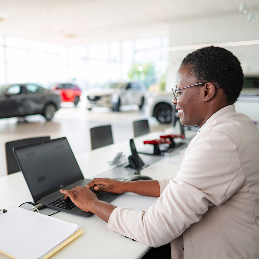 Woman typing on laptop in a car dealership