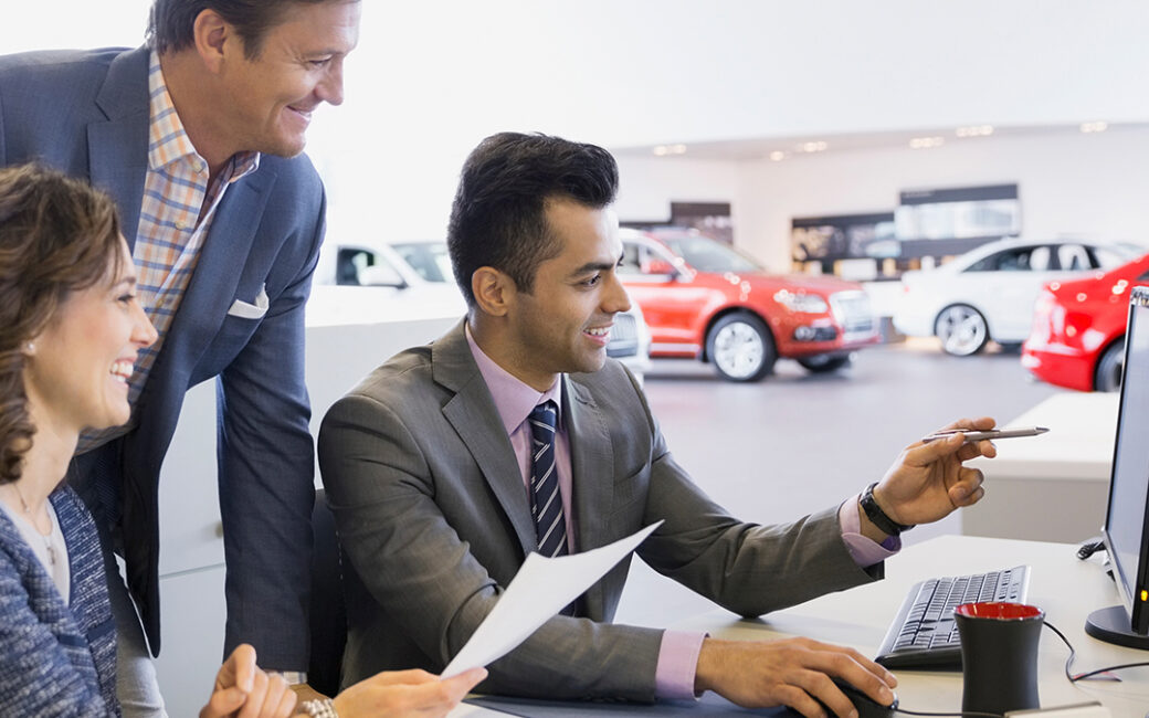Dealership employees looking at computer.