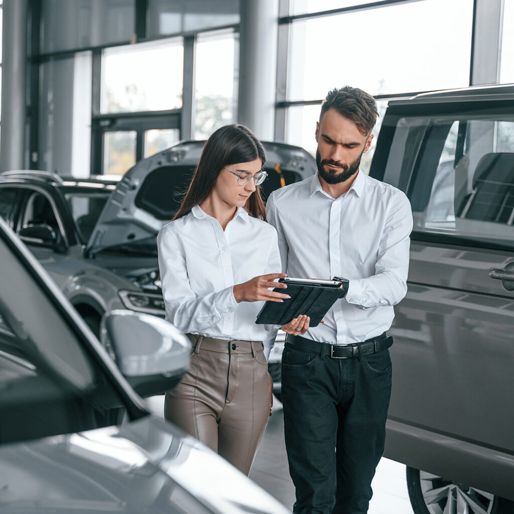 Man and woman in car dealership looking at ipad
