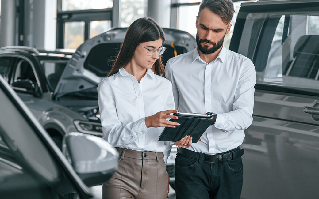 Man and woman in car dealership looking at ipad