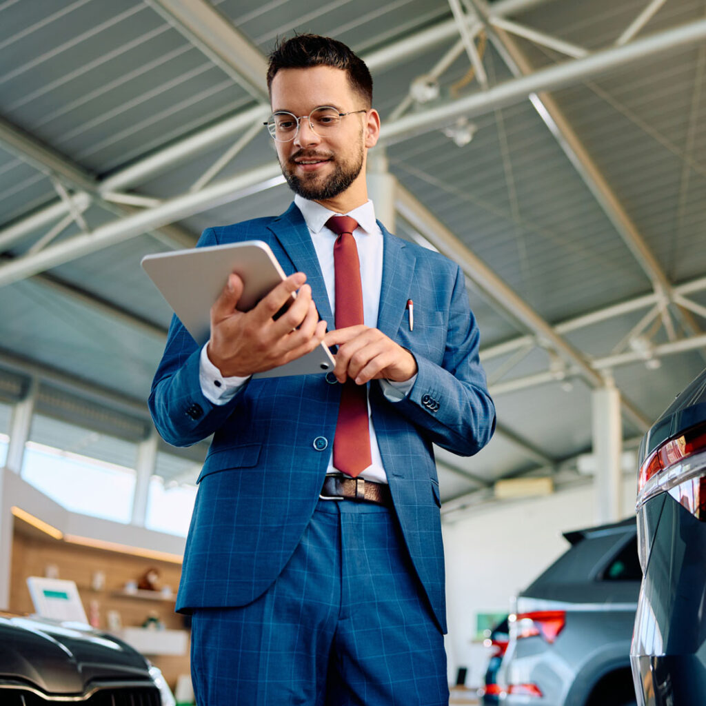 Car salesman working on digital tablet in a showroom.